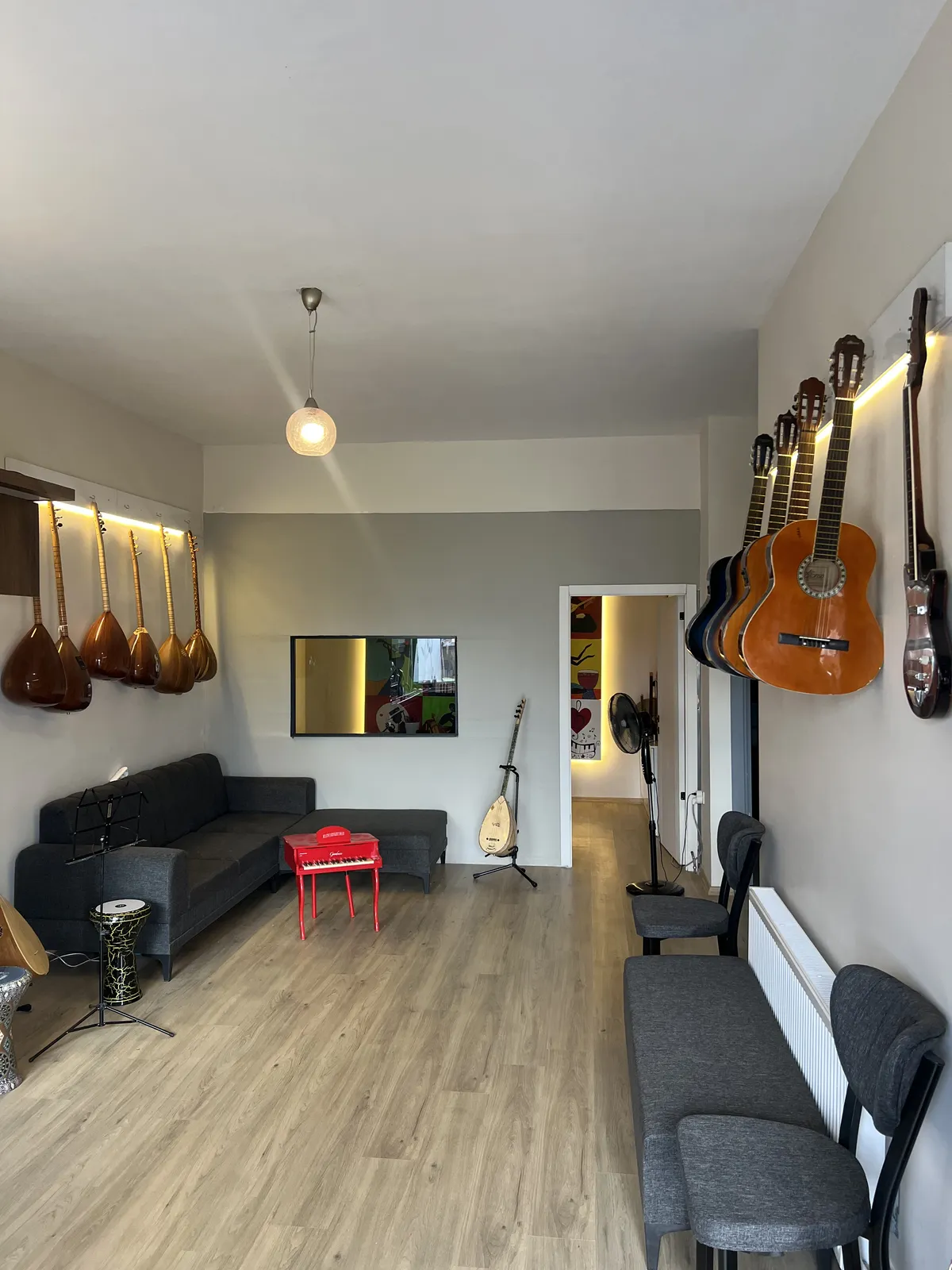 Çınar Müzik ders salonu: duvarda LED ışıkla aydınlatılmış bağlamalar ve gitarlar, açık ahşap zemin